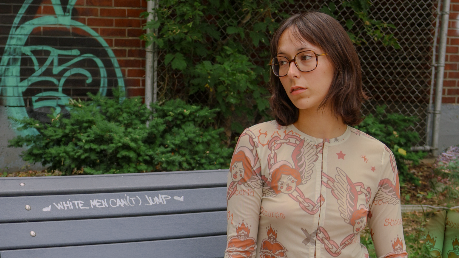 Woman sitting on a bench in an urban setting with graffiti in the background
